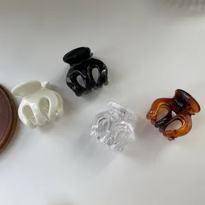 Detail of four transparent minimalist hair claws in cream, black, clear and amber tones