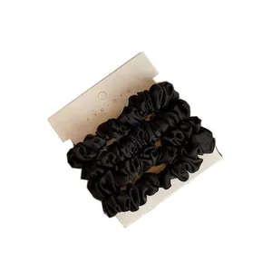 Set of four black pleated silk satin scrunchies displayed on a retail white card
