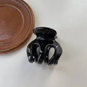 Glossy black hair claw clip for French twist on a minimalist beige desk background