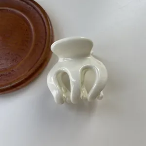 Close-up of cream-colored claw clip with a smooth resin finish on a minimal gray background