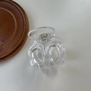 Detailed top view of a clear acrylic hair claw clip with visible metal spring on a tray
