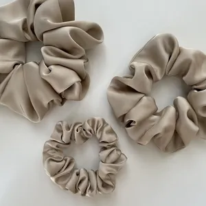 Detailed view of three champagne gold satin scrunchies in various sizes with silk texture