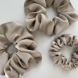 Three sizes of champagne satin scrunchies with elegant silk texture on white background