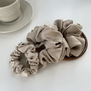 Elegant champagne satin hair scrunchies set with a silky finish on a wooden coaster
