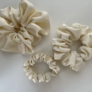 Close-up of three various sized ivory satin scrunchies with smooth silky texture