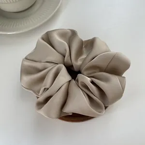 Macro detail of glossy champagne satin scrunchie showing smooth fabric texture and pleats