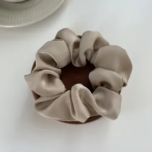 Close-up of a silky champagne satin scrunchie on a wooden tray with soft lighting