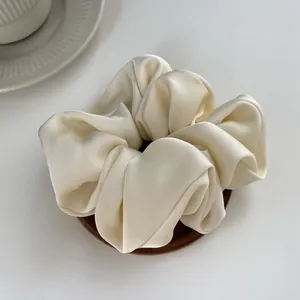 Detailed view of large cream satin scrunchie with silky texture on white tray