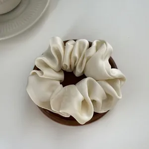 Detailed view of a creamy satin scrunchie with silky folds on a wooden tray