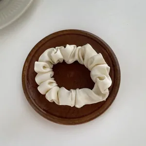 Close-up of cream satin scrunchie with silky pleated texture on a wooden tray