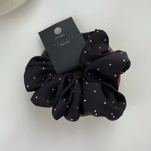 Detail view of black satin scrunchie with rhinestones on a wooden display tray