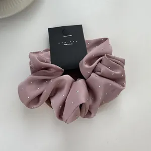 Detail of dusty pink satin scrunchie featuring delicate silver rhinestones and brand tag