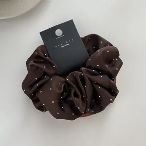 Macro detail of dark brown satin scrunchie with rhinestones and brand packaging card