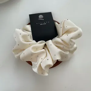Detail of cream satin scrunchie with sparkling rhinestones on a wooden stand