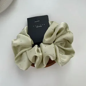 Macro detail of a light green satin scrunchie with rhinestones on a white background