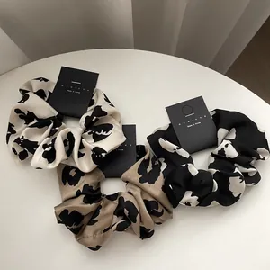 Three premium floral and leopard print scrunchies displayed on a minimalist white table