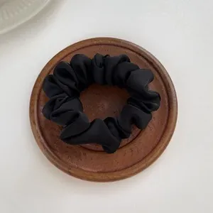 Glossy black satin scrunchie with pleated design on a minimalist wooden tray