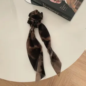 Detalle de coletero tie-dye marrón oscuro con cintas largas sobre escritorio blanco