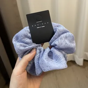 Detailed texture of lavender lace scrunchie fabric with a premium brand tag