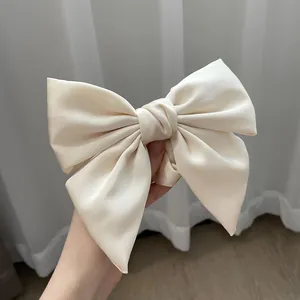 Large cream satin bow hair tie with silky texture held by hand to show premium size
