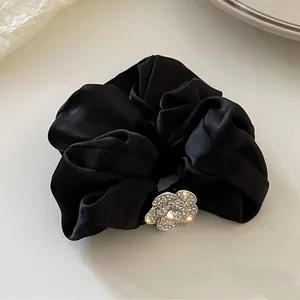 Dettaglio di un elastico in raso nero con un fiore di camelia scintillante con strass