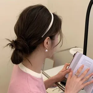 Elegant white knotted headband and pearl hoop earrings worn by woman reading a book