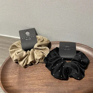 Elegant velvet hair scrunchies with diamond accents in black and beige on a wooden tray