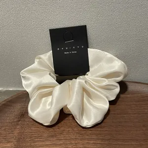 Detail of cream white satin scrunchie with rich pleats on a wooden tray with a black tag