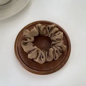 Silky dark coffee satin scrunchie with cream texture on elegant wooden tray