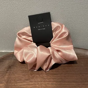 Close-up of pink satin scrunchie on a wooden tray with a minimalist brand tag