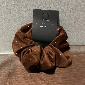 Close-up of a brown velvet scrunchie with white pearl dots on a wooden stand