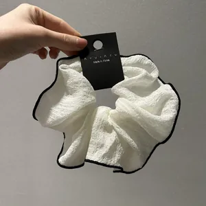 Λεπτομέρεια από λευκό scrunchie με μαύρη άκρη πάνω σε κάρτα προϊόντος από την Κορέα