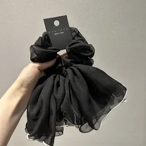 Détail d'un chouchou en mousseline noire avec bordure festonnée blanche et ruban satin
