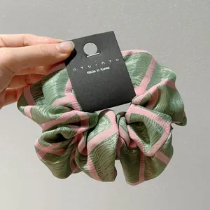 Λεπτομερής προβολή σατέν scrunchie με πράσινες και ροζ ρίγες και κορεατική ετικέτα