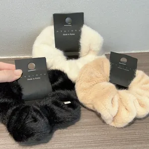 Dettaglio di tre elastici per capelli in pelliccia sintetica nero, bianco e beige