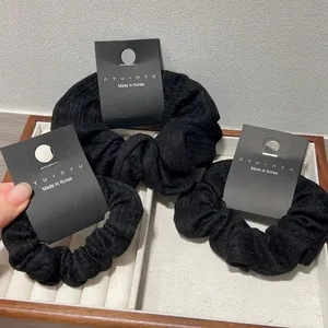 Close-up of three black ribbed fabric scrunchies on a wooden tray with brand tags