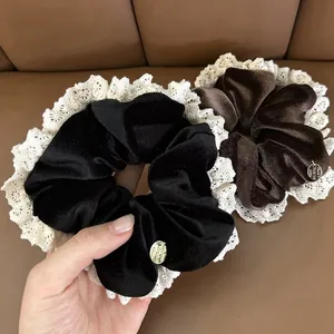 Close-up of velvet scrunchies with lace trim and gold metal tags in hand