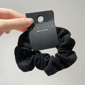 Detail of a black striped knit hair scrunchie displayed on a paper card with branding