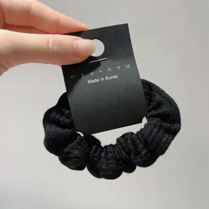 Detail of black striped knit fabric scrunchie displayed on a premium brand card