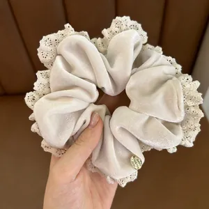 Detail of beige velvet scrunchie with delicate lace edges and gold metal tag