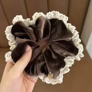 Detailed shot of brown velvet scrunchie with beige lace trim and gold metal tag charm