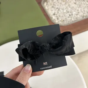 Detail of elegant black velvet bow hair clip with chic pleated texture on display card