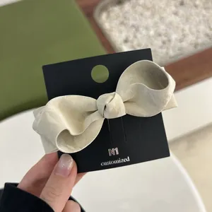 Close-up of a cream bow hair clip in textured faux leather on a black display card