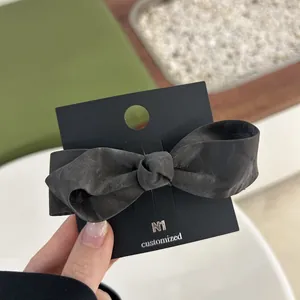 Close-up of elegant dark grey bow hair clip with matte texture on a display card