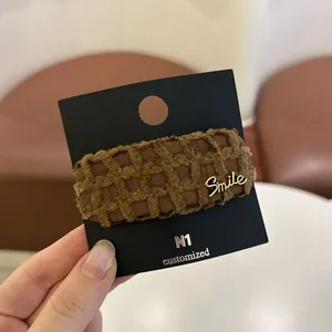 Detail van een bruine stoffen haarclip met een gouden Smile-embleem op een kaart