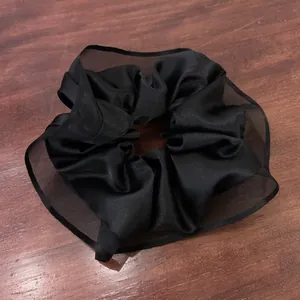 Detail of large black satin scrunchie with sheer mesh trim on a dark wooden background
