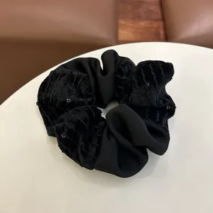 Λεπτομέρεια μαύρου βελούδινου scrunchie με πούλιες και πλισέ ύφασμα σε δερμάτινο φόντο
