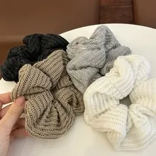 Detail of four knit hair scrunchies in black, grey, beige, and cream with ribbed texture