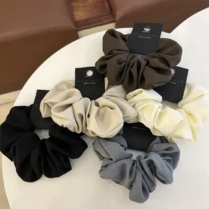 Five solid color fabric scrunchies set in earth tones on a white table surface