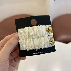 Λεπτομέρεια από κλιπ μαλλιών σε κρεμ λινό με φθαρμένες άκρες και χρυσούς φιόγκους